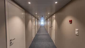 A long, narrow hallway with doors on both sides, leading to a bright room at the end.