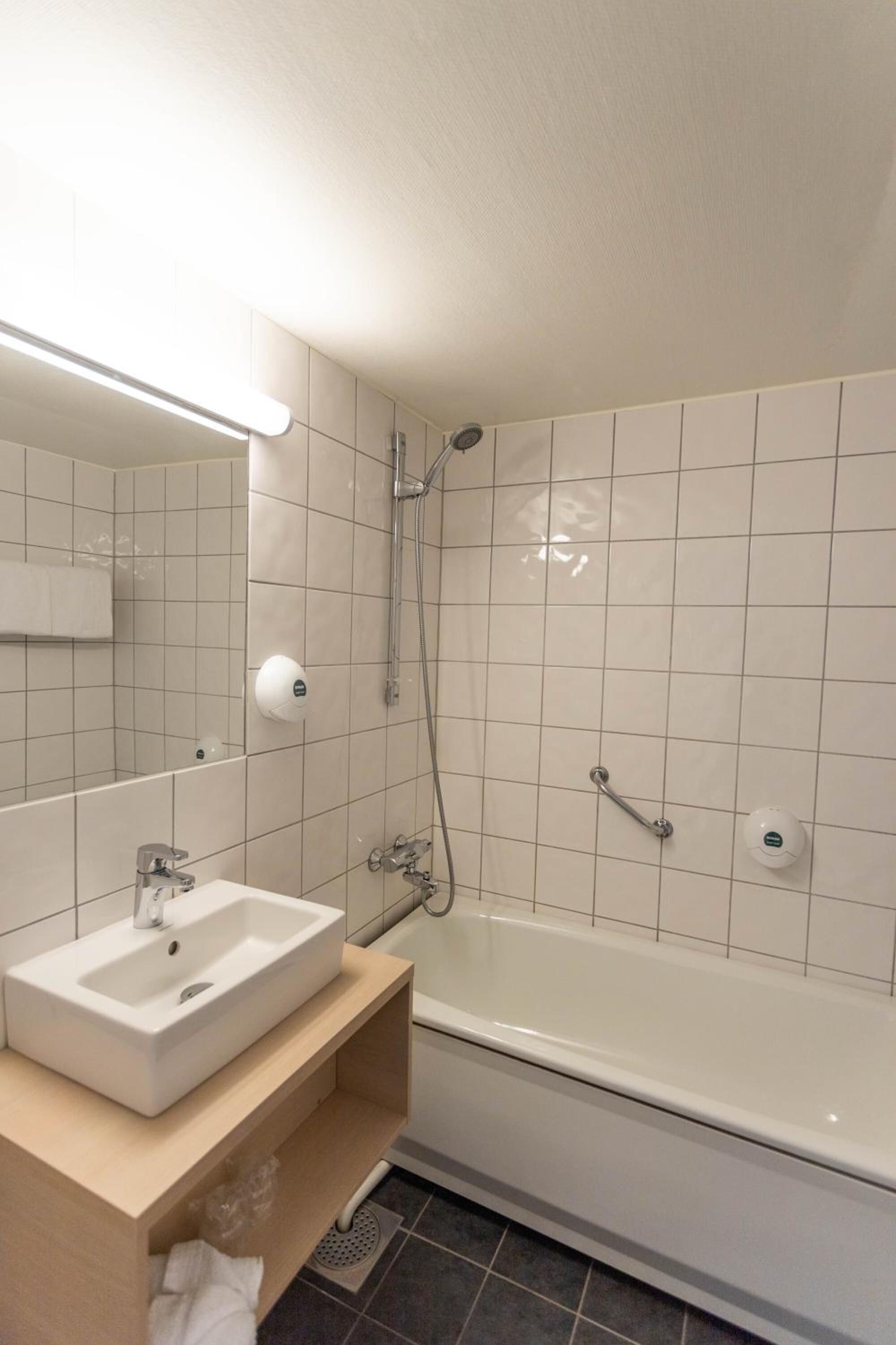 Un baño moderno con lavamanos, espejo y bañera blancos.