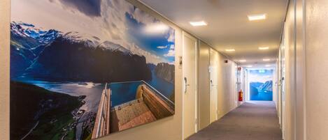 A hotel corridor with a large mural of a mountainous landscape and a dam.