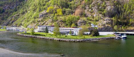 Järvenrantahotelli, jossa on moderni rakennus, laituri ja taustalla kivinen rinnemäki.
