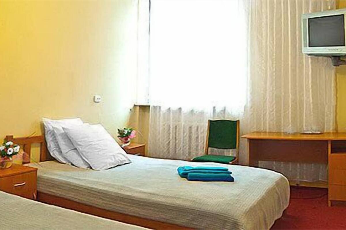 A hotel room with two beds, a desk, a television, and a window with curtains.