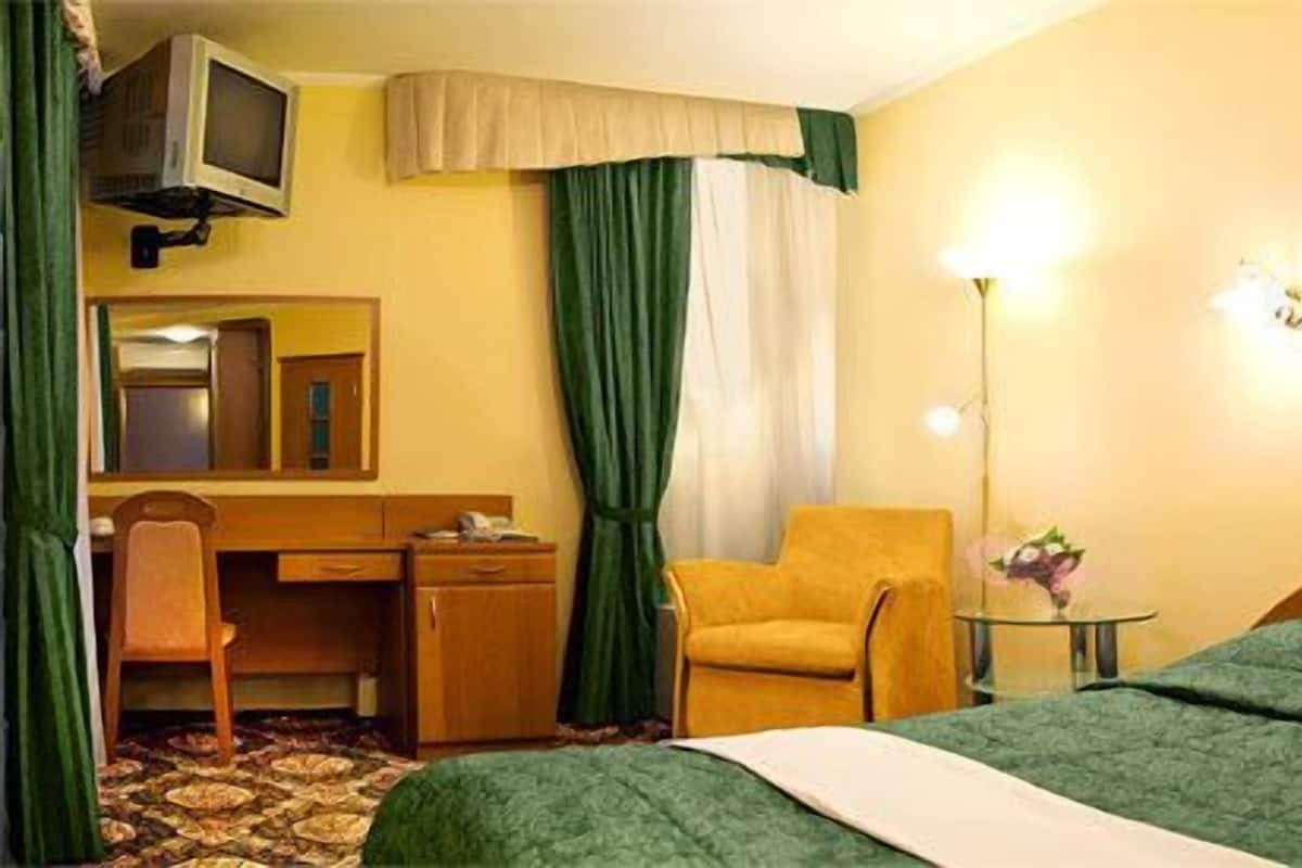 A hotel room with a bed, a desk, a chair, a television mounted on the wall, and a painting on the wall.