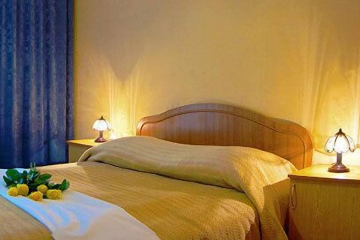 A hotel room with a bed, two bedside lamps, a chair, a desk, and a window with curtains.