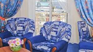 Um quarto com duas poltronas estampadas, uma mesinha com um vaso de flores e um abajur sobre uma mesinha de madeira.