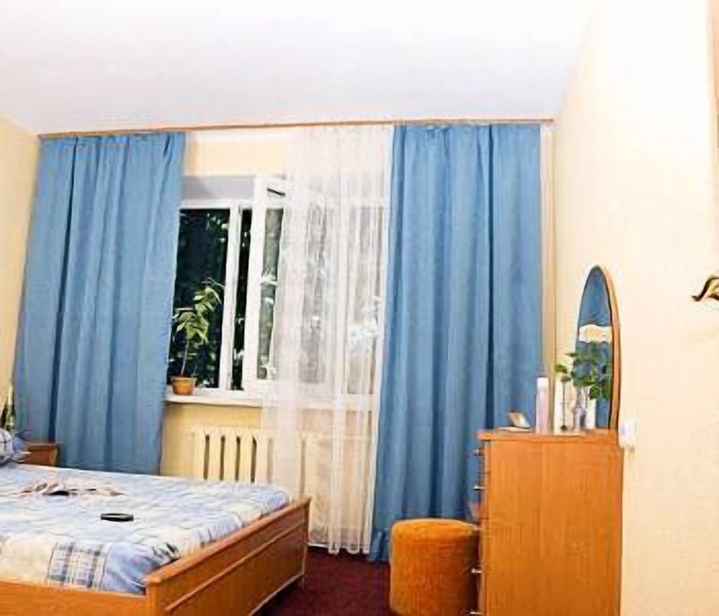 A bedroom with a bed, a dresser, a window with curtains, and a radiator.