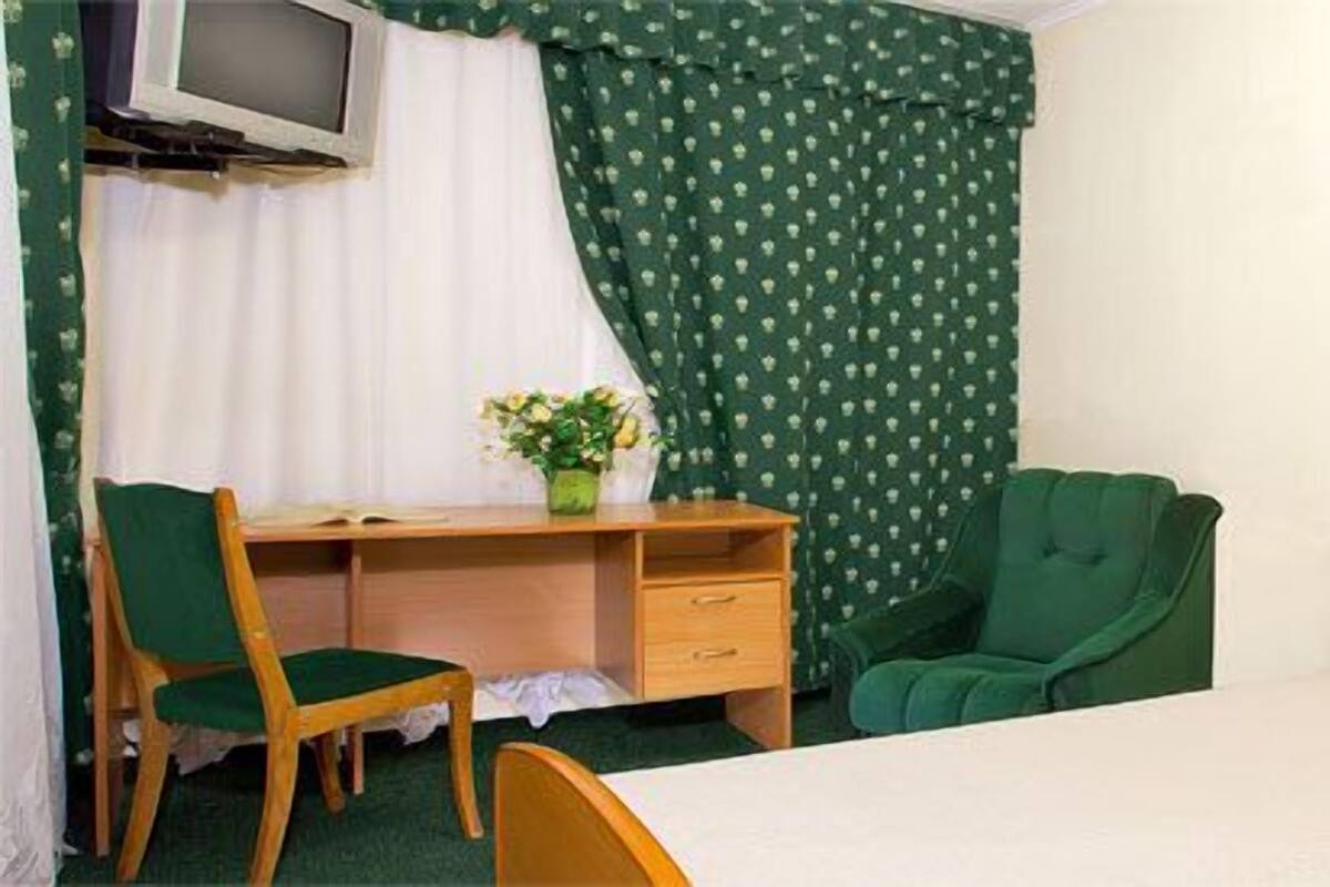 A hotel room with a bed, a desk with a chair, a TV, and a small table with a vase of flowers.