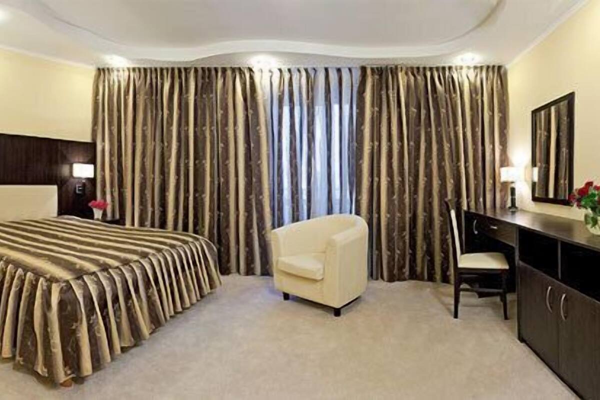 A hotel room with a large bed, two armchairs, a desk, and a dresser.