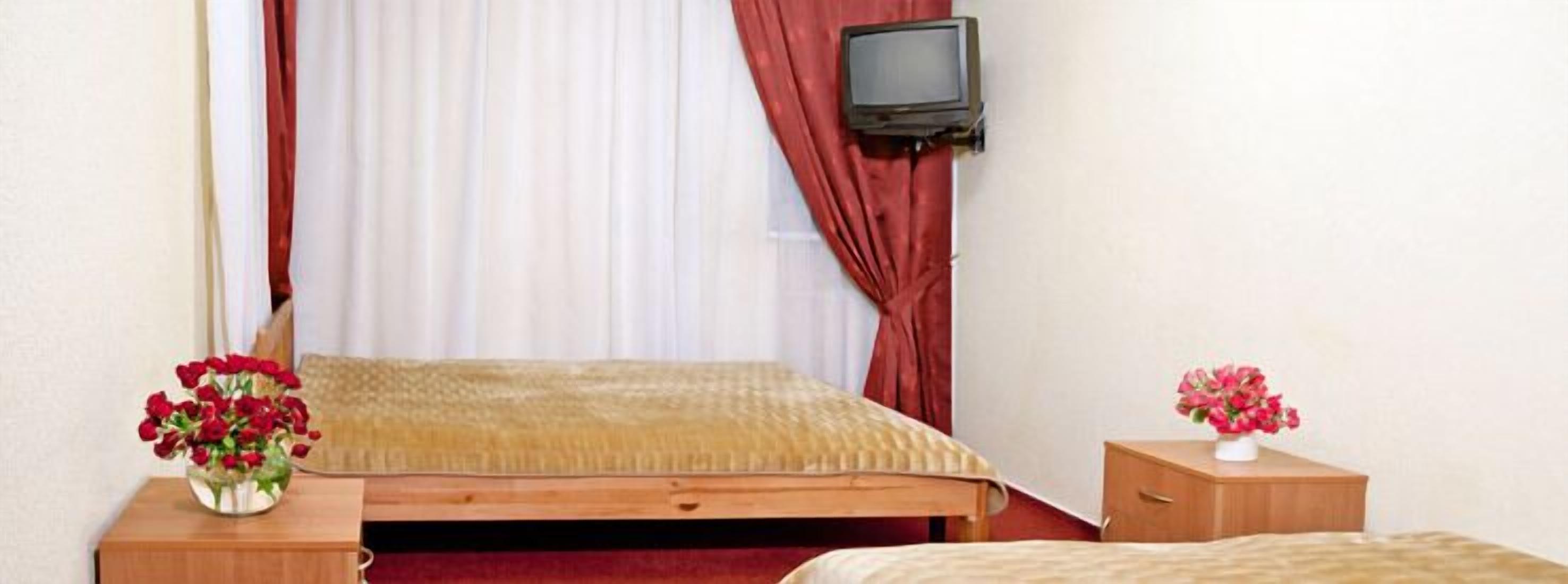 Una camera d'albergo con un letto, una televisione montata a parete e due comodini con vasi di fiori.