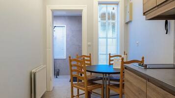 A small dining area with a round table and four wooden chairs, a built-in wooden cabinet, and a window with blinds.