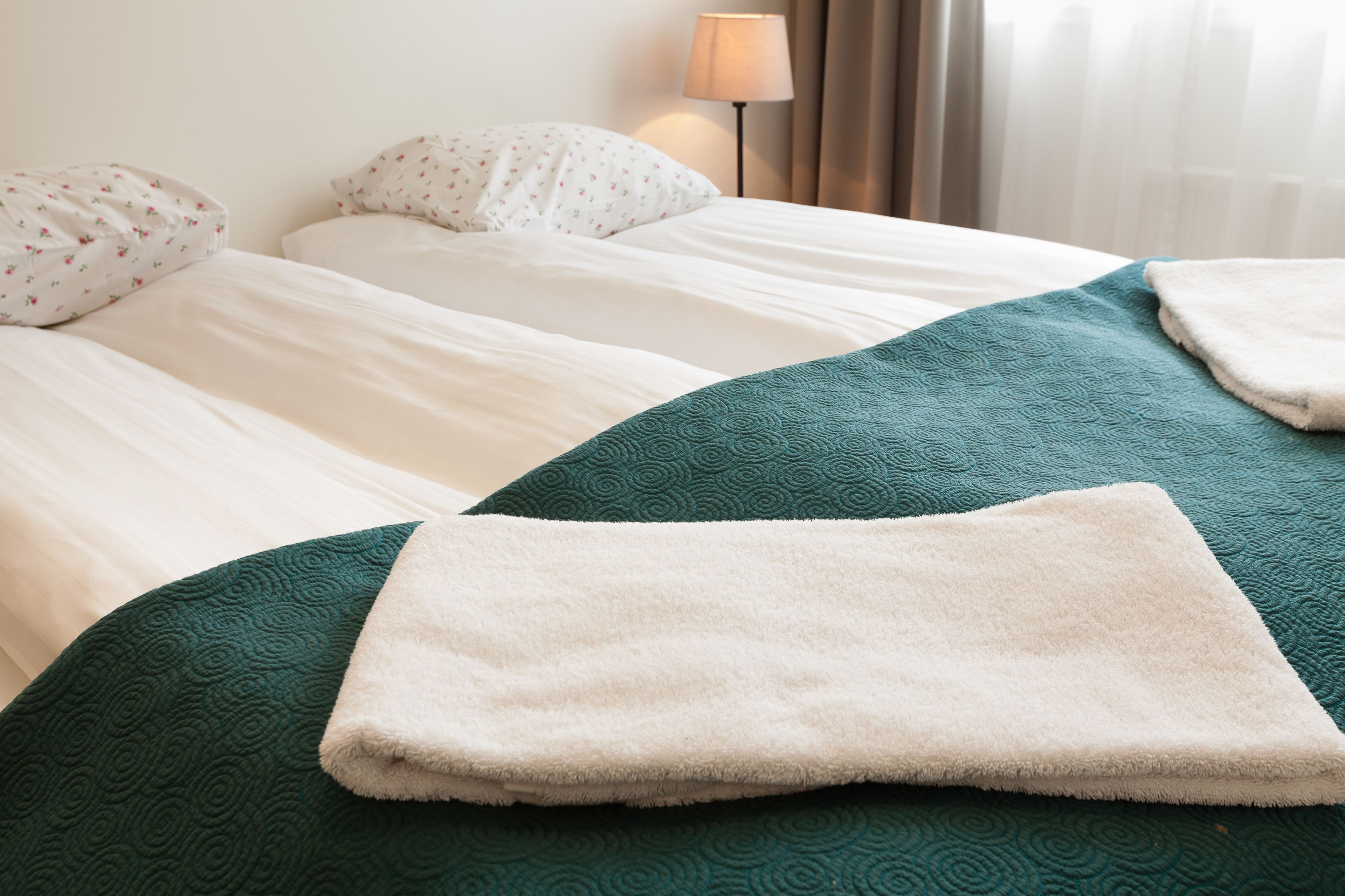 A hotel room with two beds, a green textured bedspread, white pillows, and a white fluffy blanket.