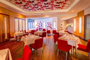A restaurant with red chairs and white tables, a wooden floor, and a ceiling with a geometric pattern. - Mantra Charles Hotel Launceston (Launceston)