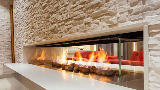 Un interior moderno con pared de piedra, encimera blanca y chimenea con fuego visible.