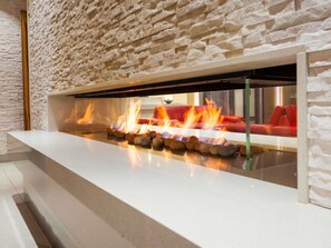 Un interior moderno con pared de piedra, encimera blanca y chimenea con fuego visible.