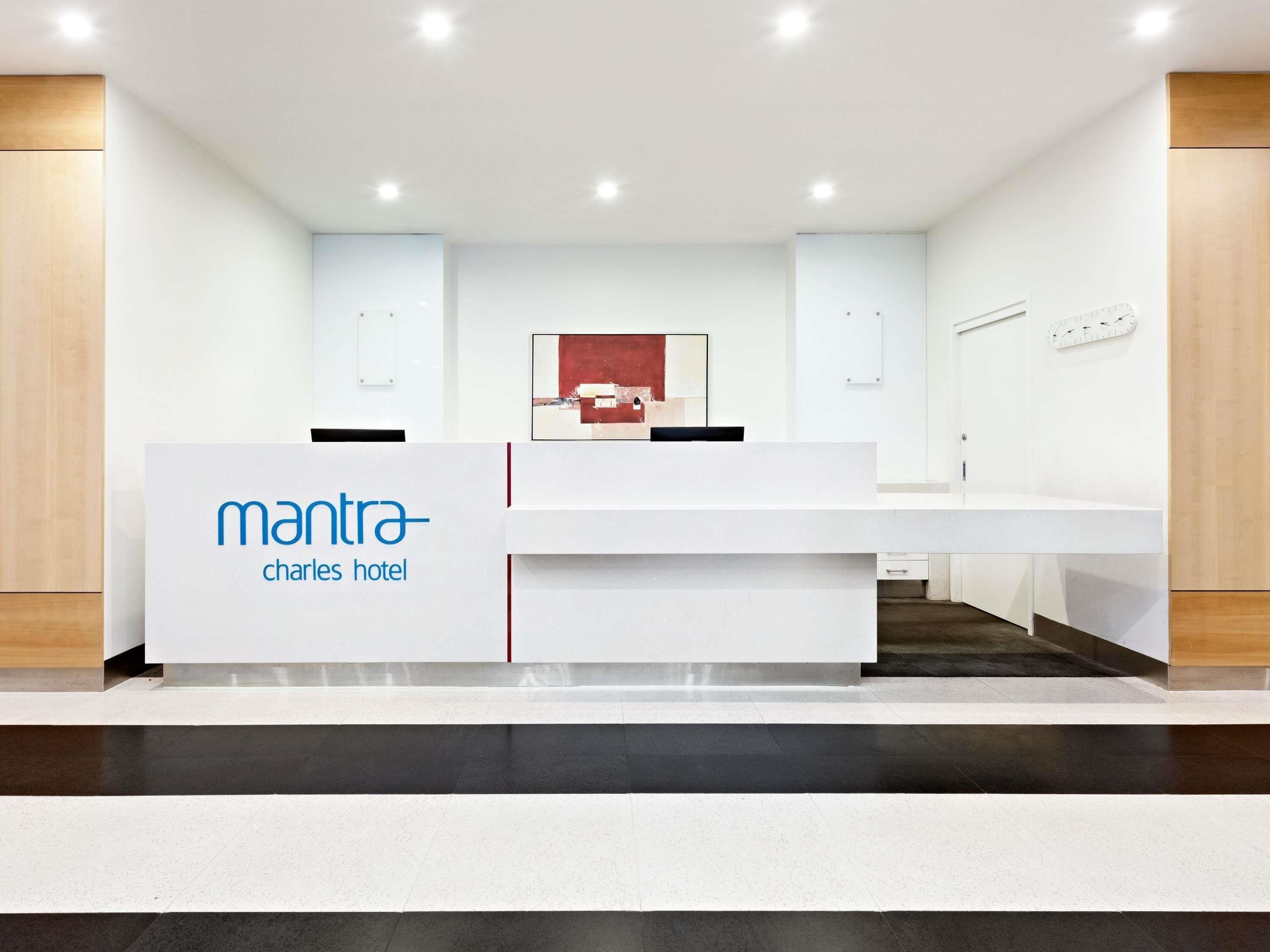 A reception desk with a sign reading 'mantra charles hotel,' a modern interior design, and a clock on the wall.