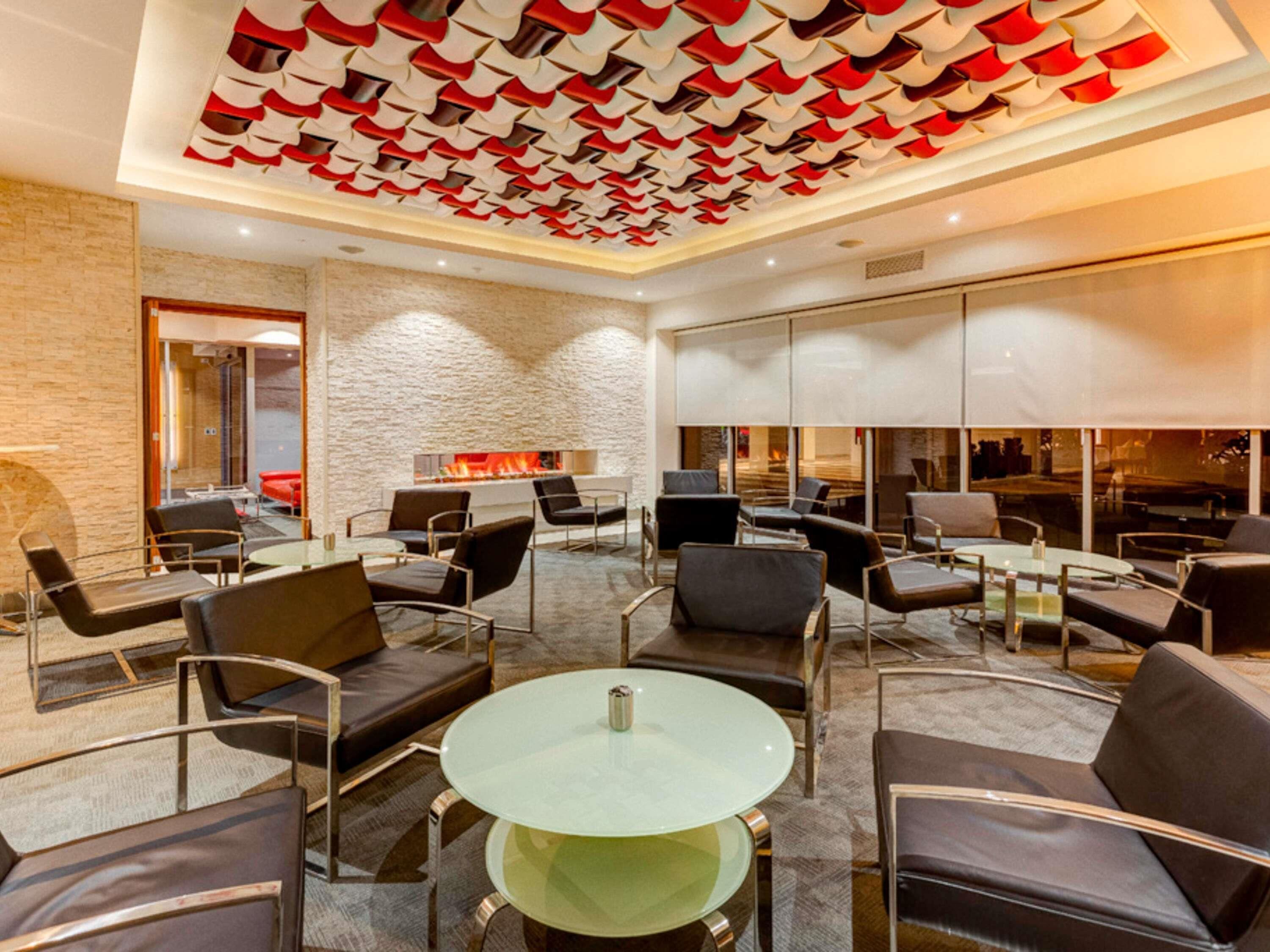 A modern lounge area with a stone wall, a fireplace, and a ceiling with a geometric pattern.