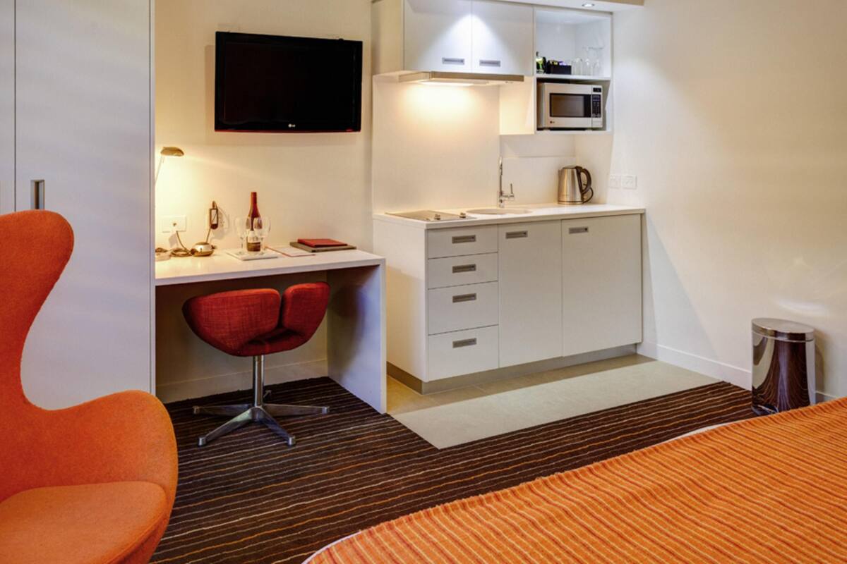 A hotel room with a bed, a desk with a chair, a television, a microwave, and a sink.