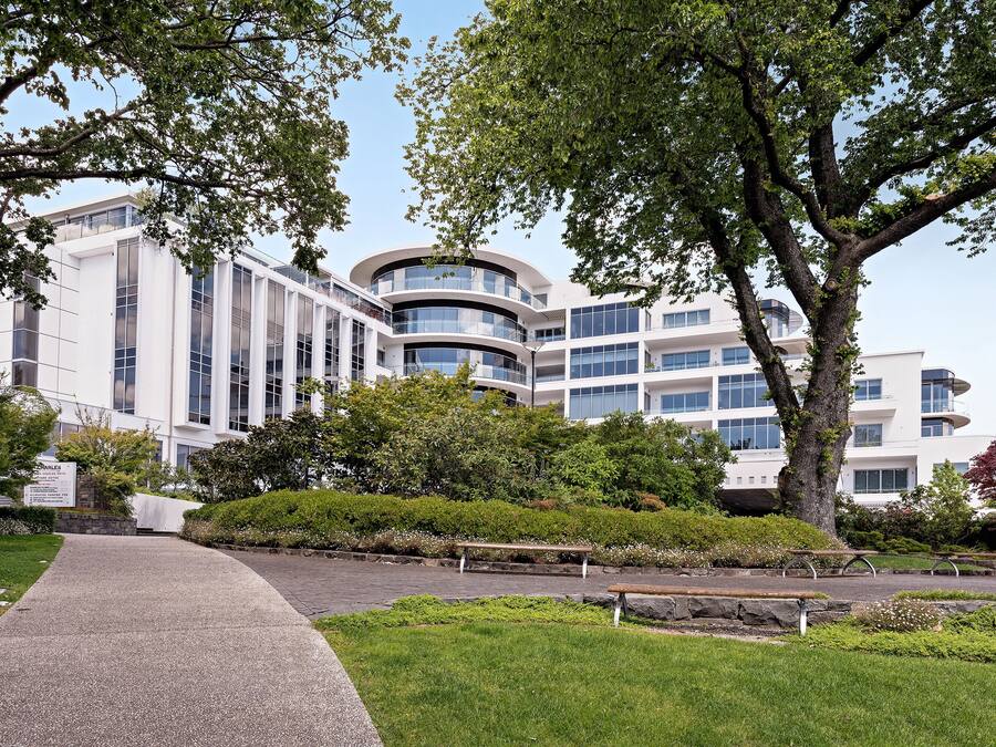 A modern building with a curved facade, surrounded by well-maintained greenery and benches.
