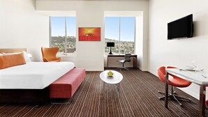 Habitación de hotel con cama, escritorio, silla, mesita y televisor.