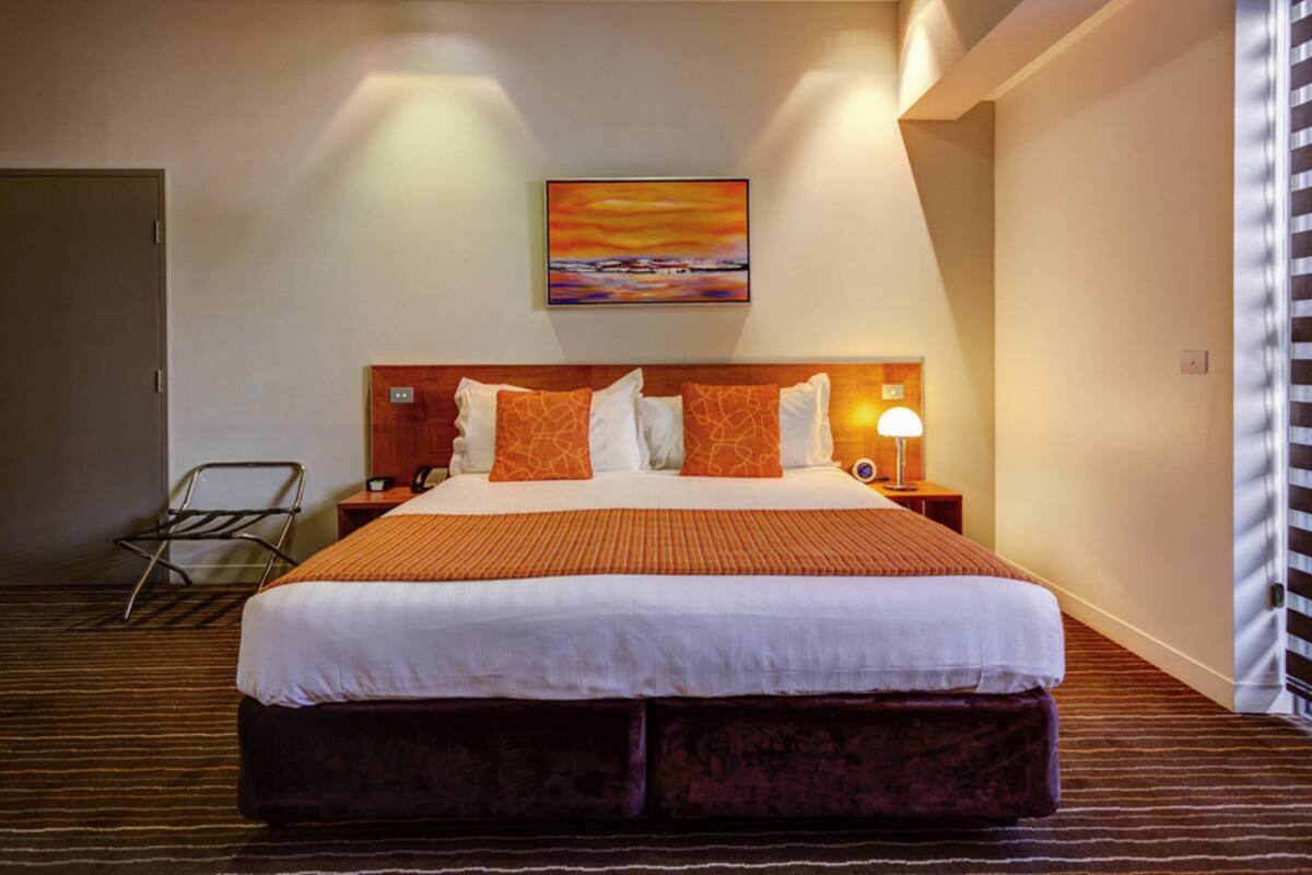 A hotel room with a large bed, a nightstand, a lamp, and a painting on the wall.