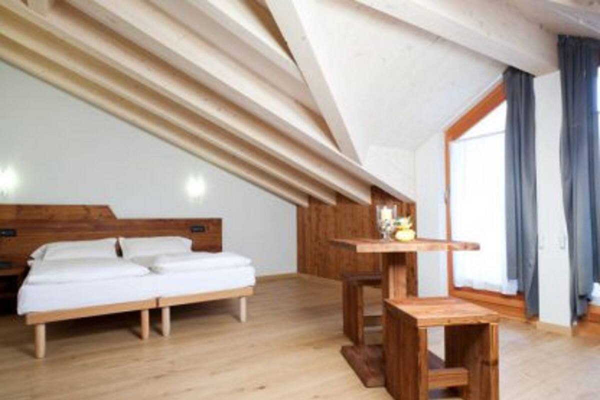 A bedroom with a wooden bed, a small wooden table, and a large window with curtains.