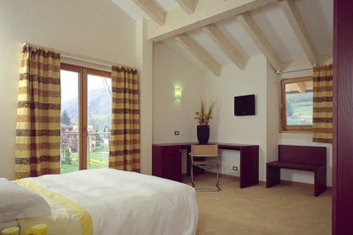 A bedroom with a bed, a desk, a chair, and a window with curtains.