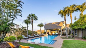 A poolside area with lounge chairs, a swimming pool, and a house with a patio. - Francolin Lodge (Mbombela)