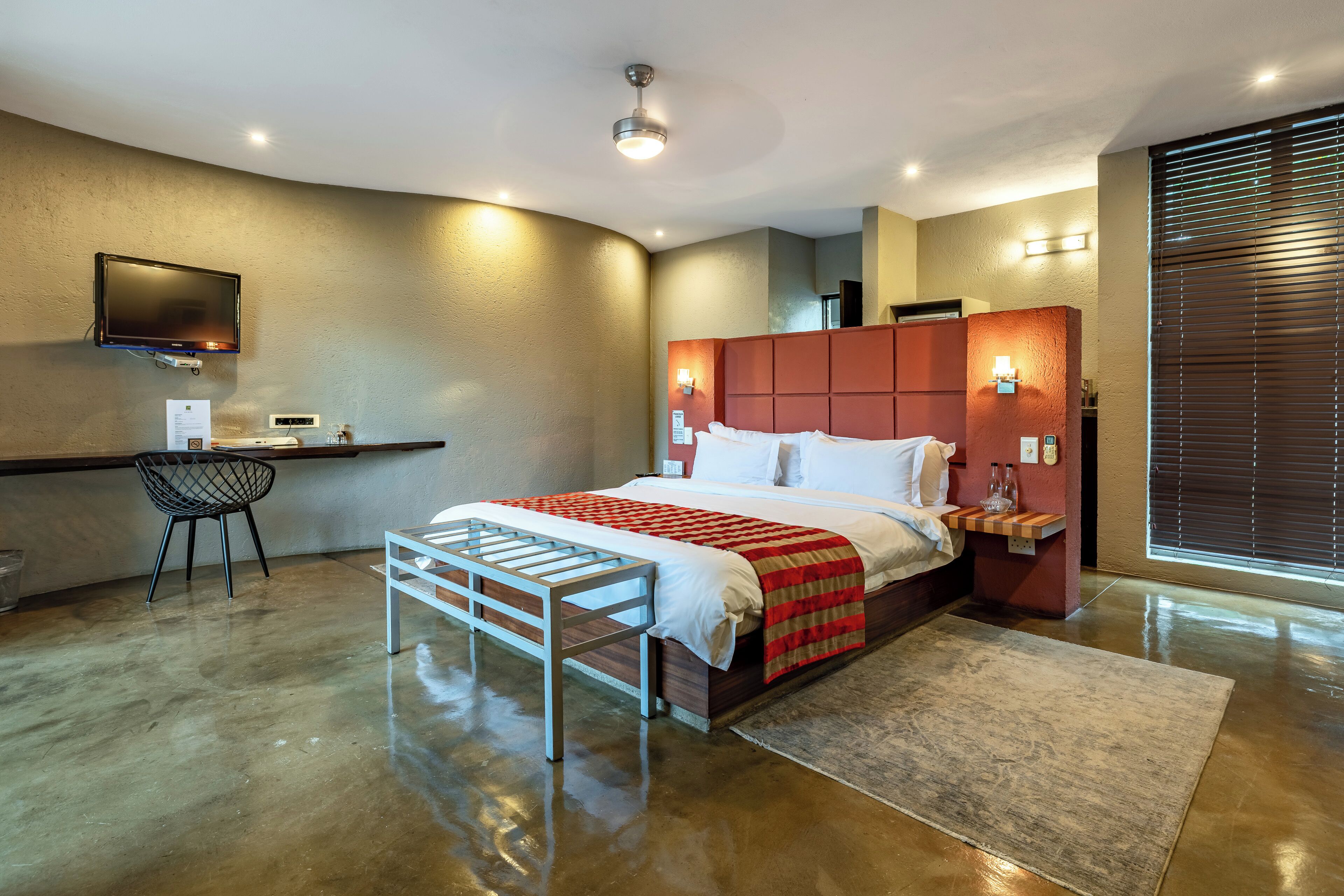 Una habitación de hotel moderna con una cama grande, un escritorio, una silla y un televisor montado en la pared.