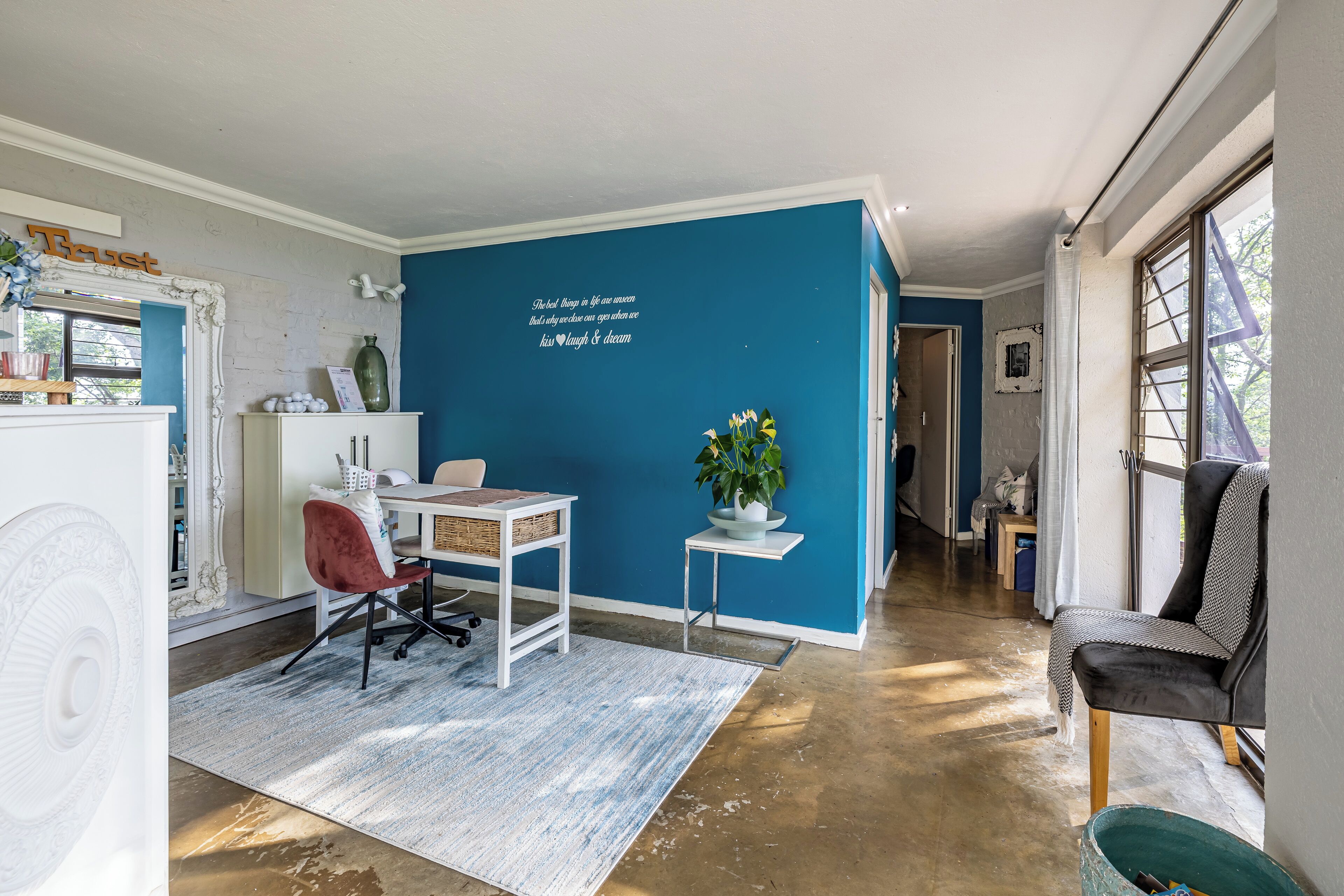 A modern living space with a blue accent wall, a white desk, a red chair, and a small plant.