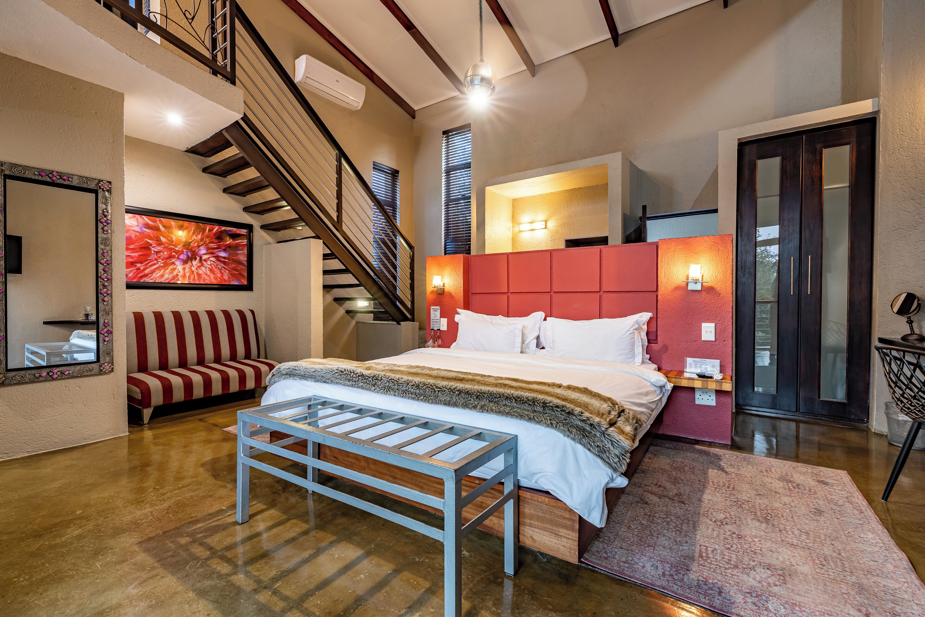 Un dormitorio con cama, un banco, un sofá, una escalera y un espejo grande.