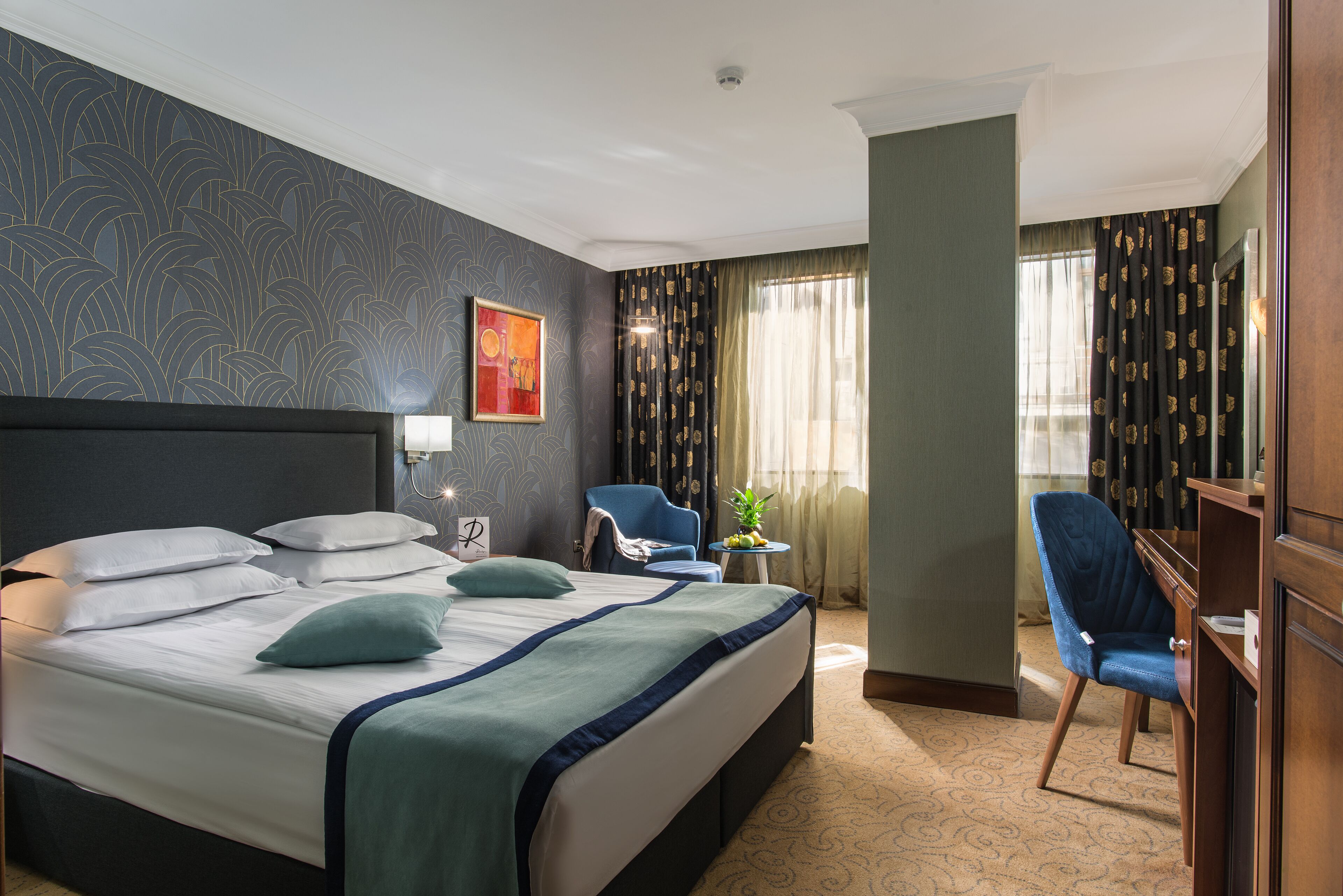 A hotel room with a large bed, a desk, a chair, and a small table with a plant.