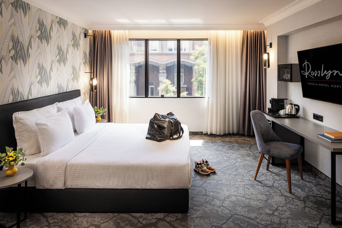 A hotel room with a bed, a desk, a chair, a TV, and a window with curtains.