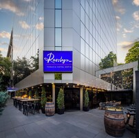 Exterior del Hotel Rosslyn Thracia Sofia, con fachada de vidrio moderna, zona de estar al aire libre y un llamativo letrero iluminado.