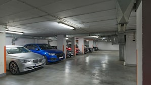Un garaje de estacionamiento con varios automóviles aparcados en filas, pisos de concreto e iluminación fluorescente.