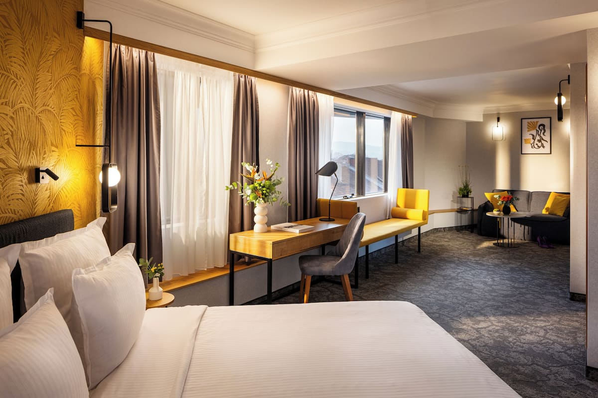 A hotel room with a bed, a desk, a chair, a sofa, and a window with curtains.