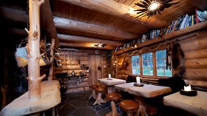 A rustic log cabin interior with a stone floor, wooden benches, a stone fireplace, and a bookshelf filled with books. - Engholm Husky Design Lodge (Karasjok)