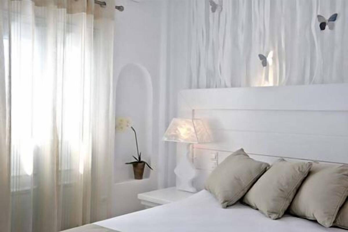 A bedroom with a bed, a bedside table, a lamp, and a potted plant.