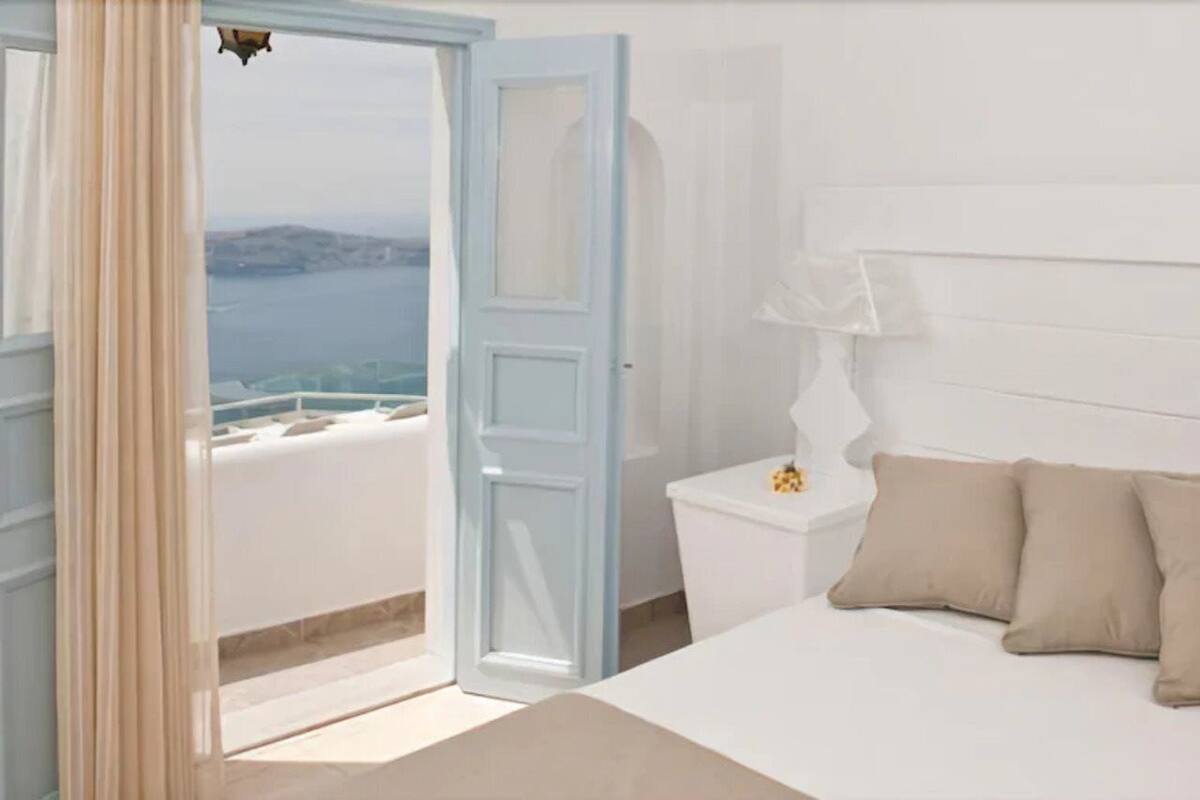 A room with a bed, a nightstand, and a view of the sea.