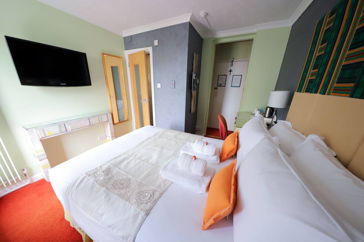 A hotel room with a bed, a flat-screen TV mounted on the wall, a door, and a lamp.