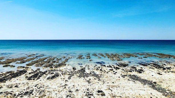 A beach with clear blue water and rocky formations. - The Cavalaire (Brighton)