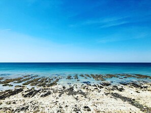En strand med krystalklart, blåt vand og klippeformationer.