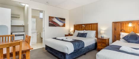 Habitación de hotel con una cama grande, una cama más pequeña, un escritorio y una silla. Hay un cuadro en la pared y una ventana.