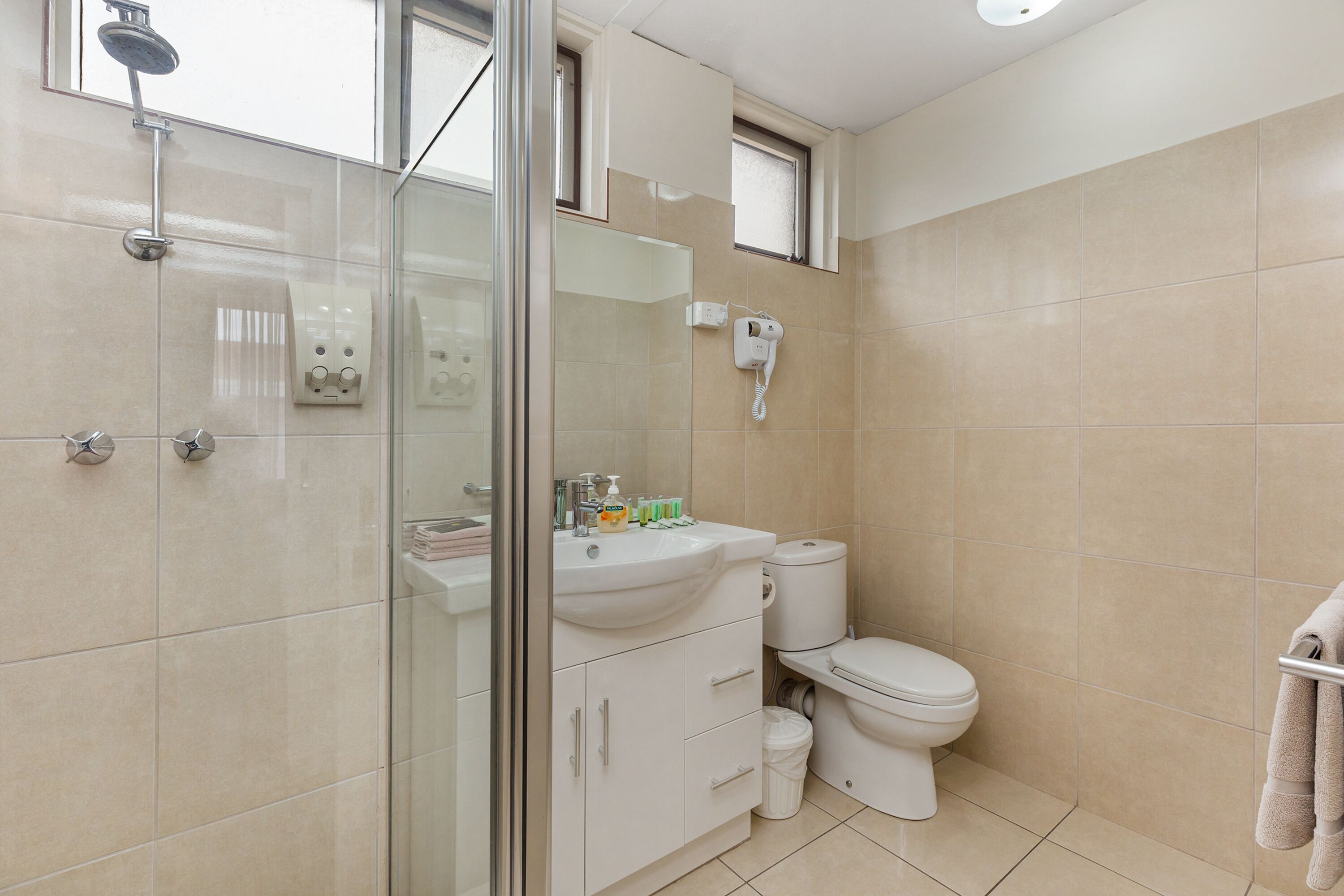 A modern bathroom with a glass shower enclosure, a white sink with toiletries, a toilet, and a towel rack.
