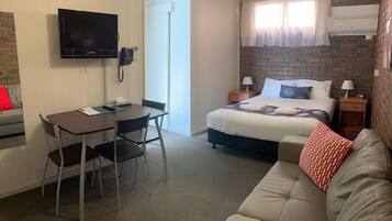 Ett kompakt hotellrum med en säng, en soffa, ett matbord med stolar, en TV och en telefon.