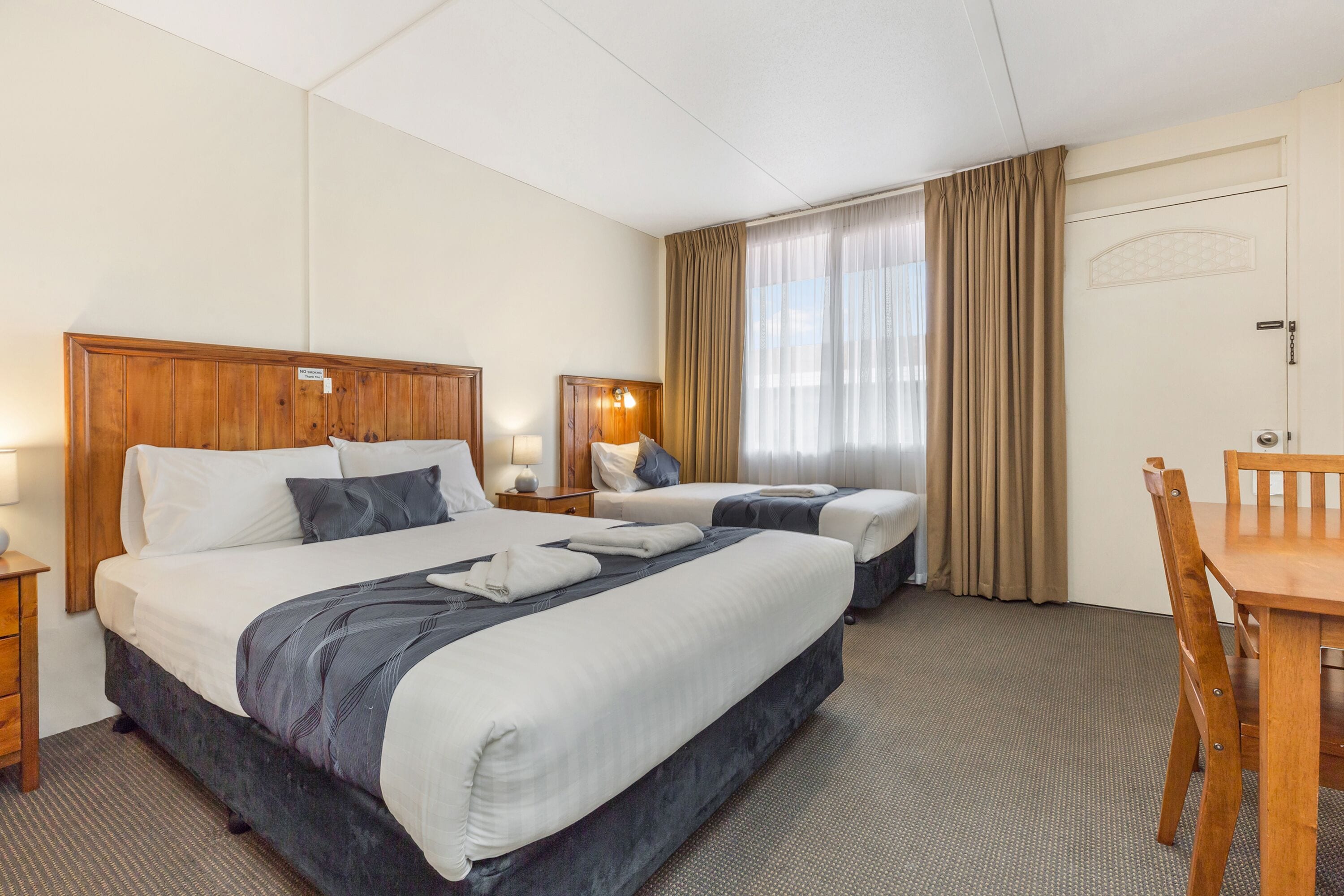 A hotel room with two beds, a wooden headboard, a desk, and a chair.
