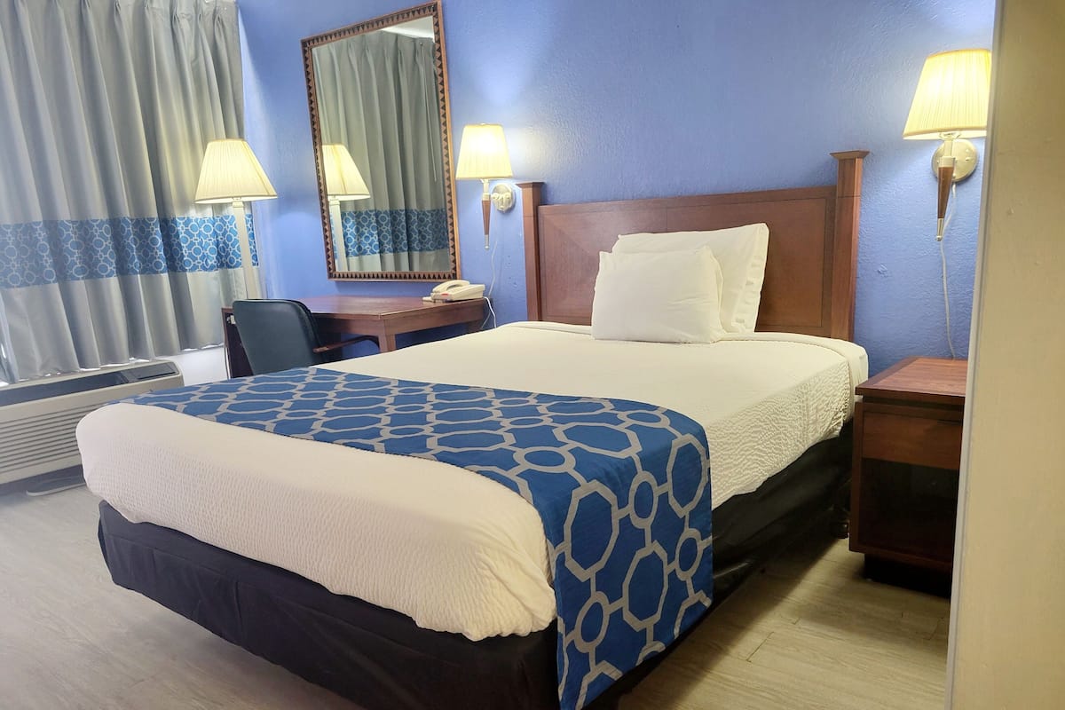 A hotel room with a large bed, a desk, a chair, a mirror, and two bedside lamps.