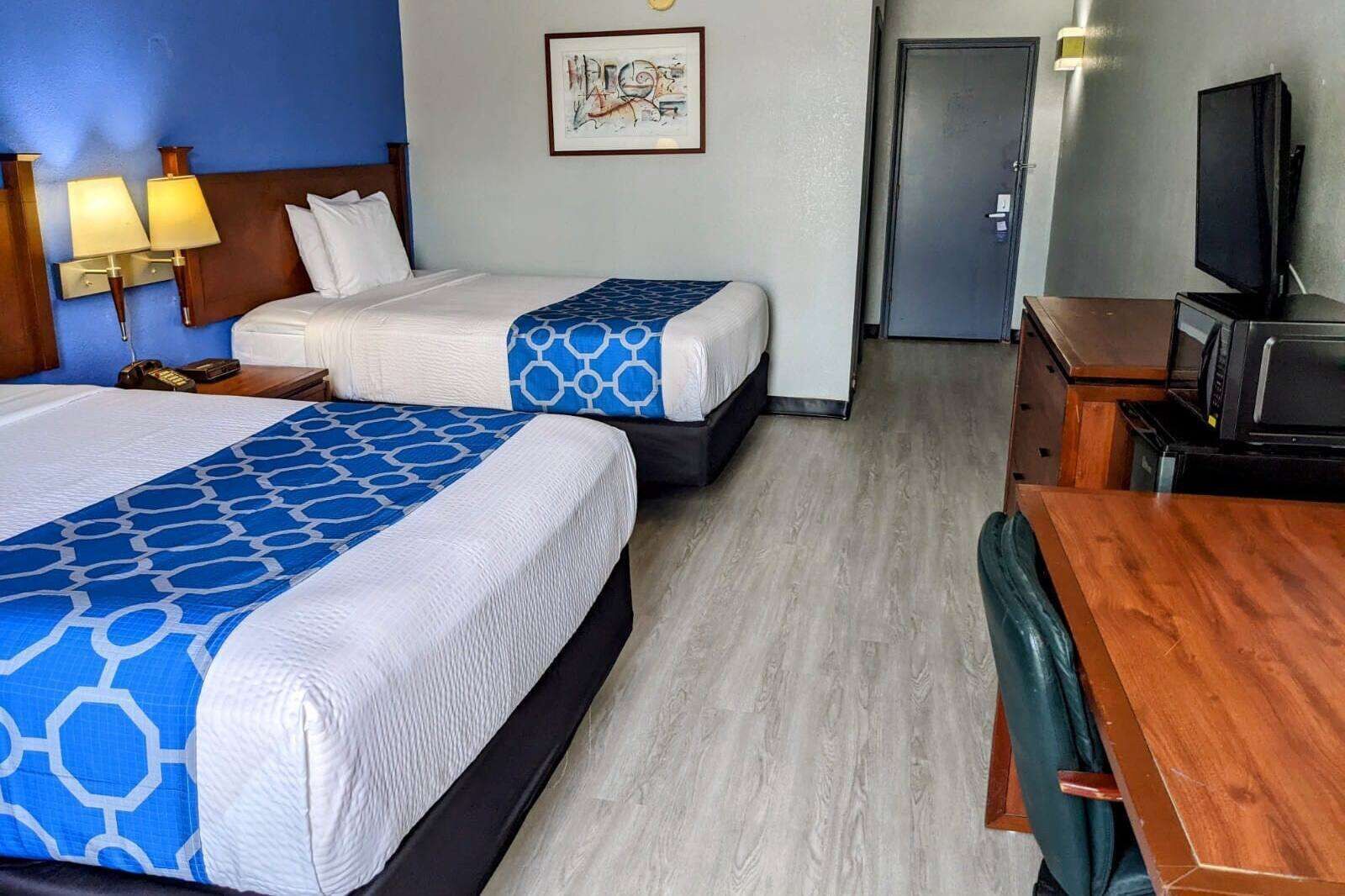 A hotel room with two beds, a desk, a television, and a door.