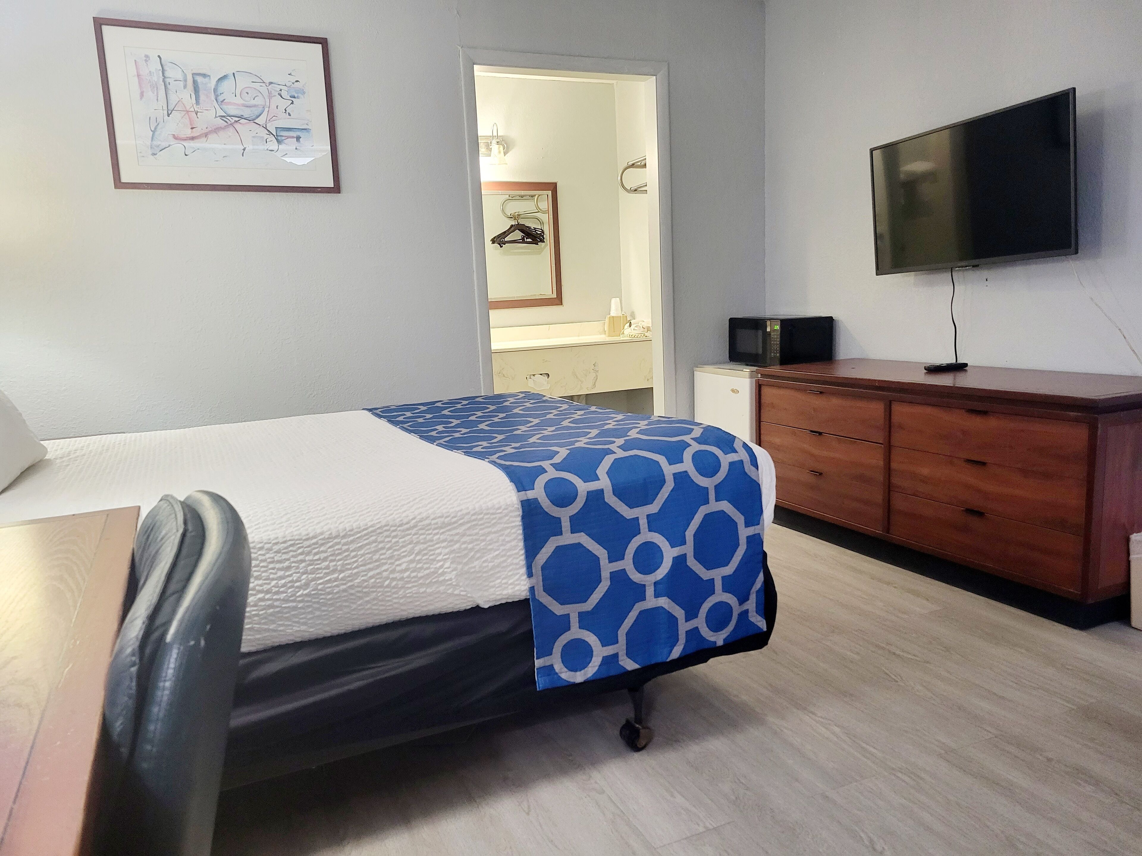 Ein Hotelzimmer mit einem Bett, einem Schreibtisch, einem Schrank, einem Fernseher und einer Tür zu einem Badezimmer.