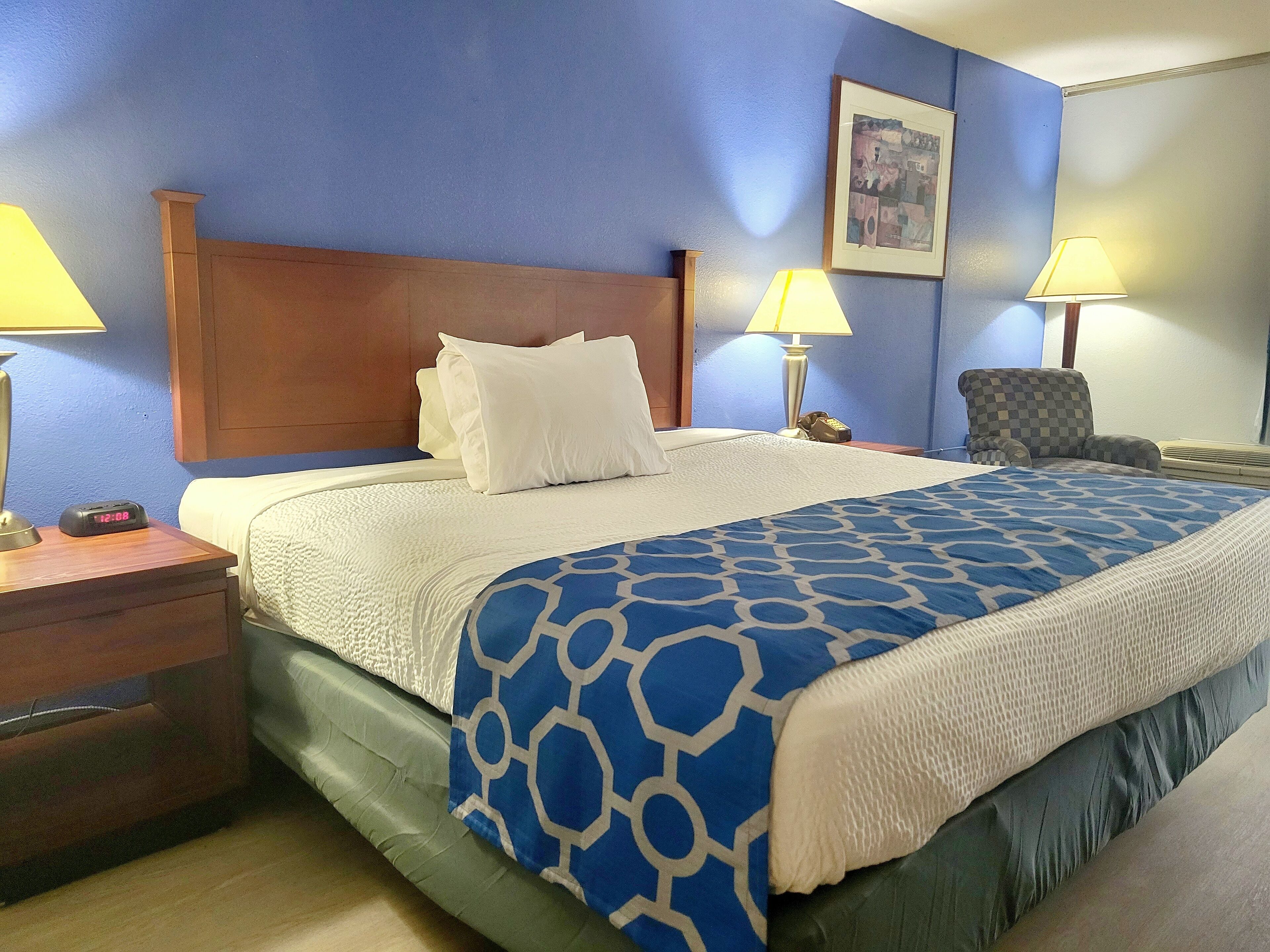 Une chambre d’hôtel avec un grand lit, deux lampes de chevet, une chaise et un tableau encadré au mur.