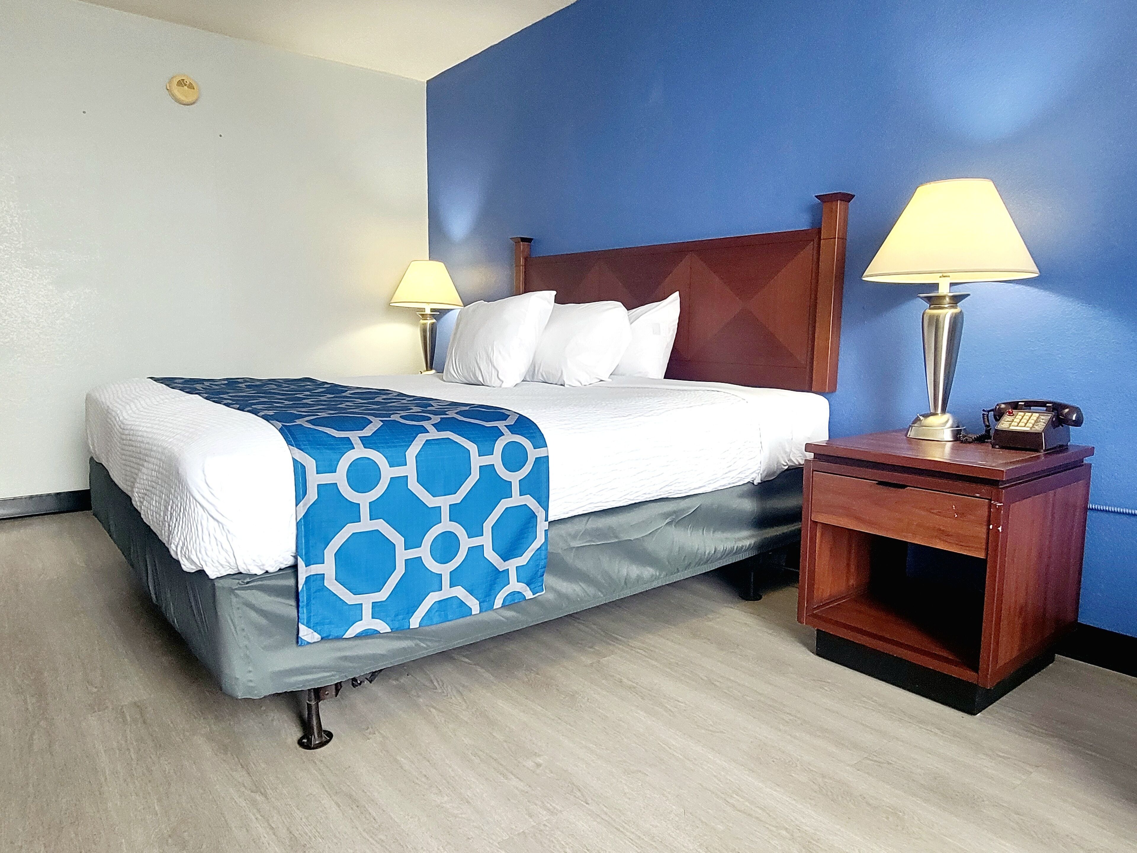 Een hotelkamer met een bed, twee bedlampen, een nachtkastje van hout en een telefoon.