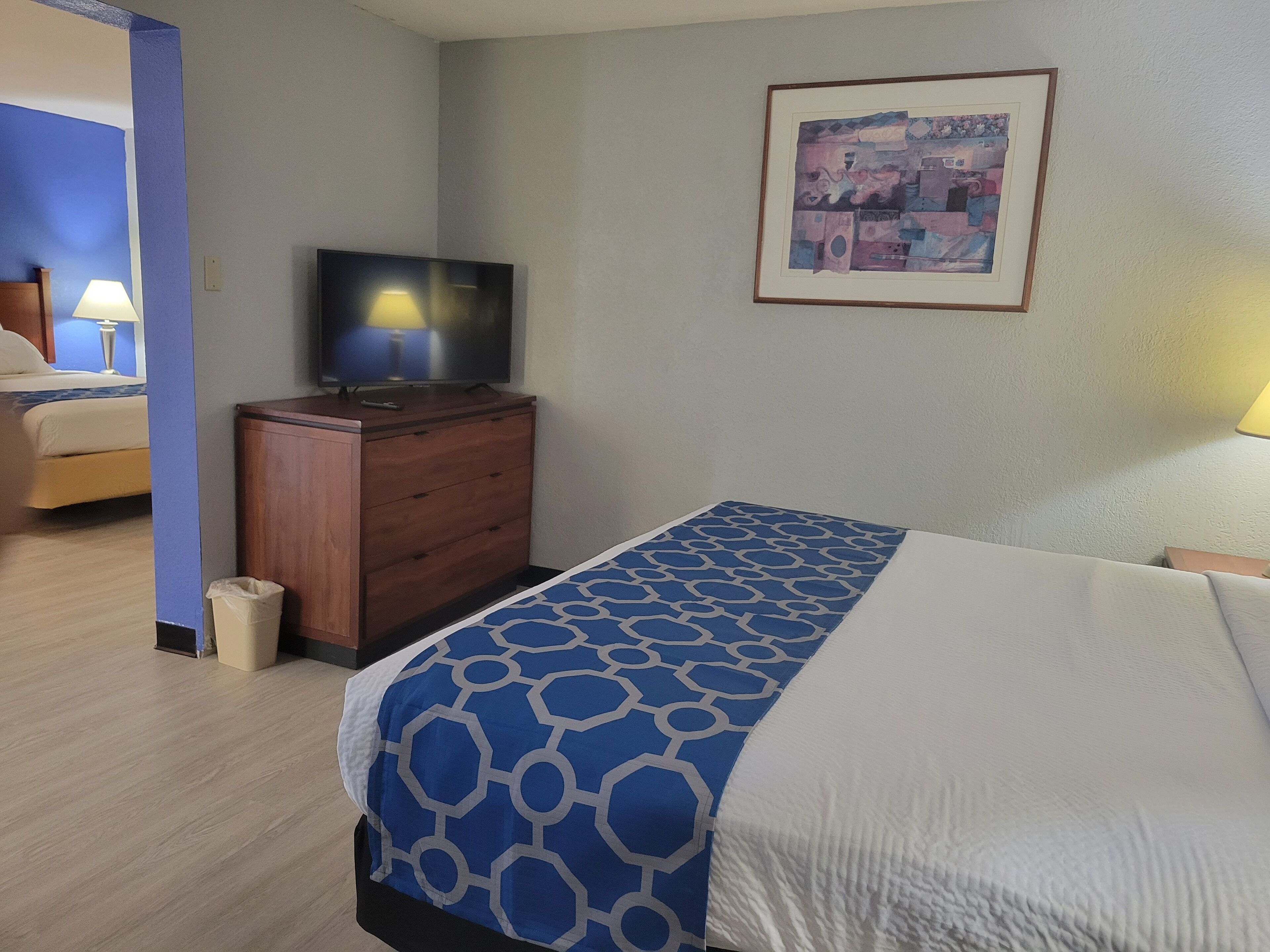 Una camera d'albergo con un letto, una cassettiera, una televisione e un quadro appeso al muro.